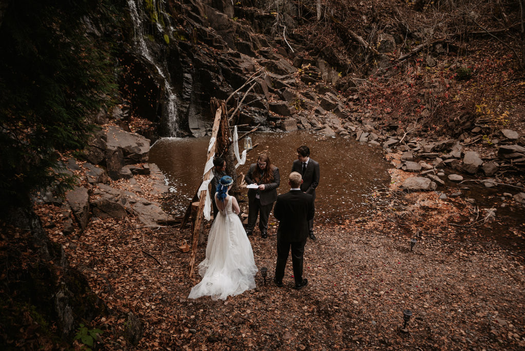 An elopement ceremony during the fall season in northern Minnesota.  The couple is exchanging vows next to a waterfall with autumn leaves surrounded them and their loved ones.