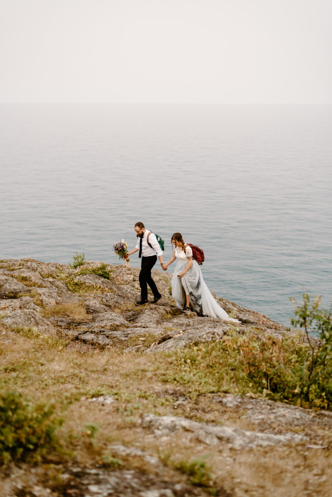 A couple walking hand in hand, along the cliff side of the north shore of Lake Superior during their summer elopement.